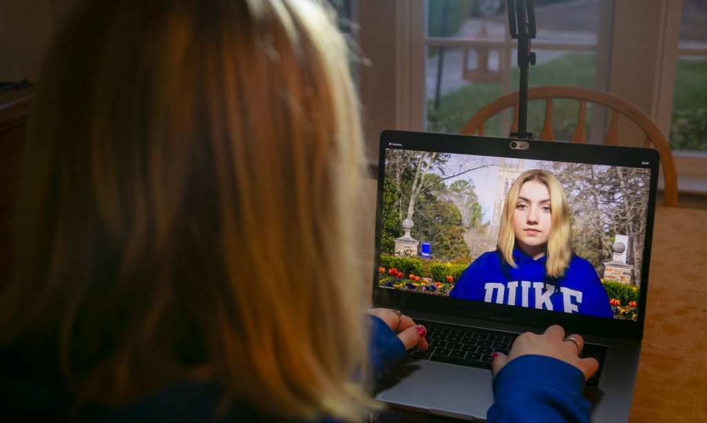 The images depicts a young woman sitting in front of a laptop for video conferencing.